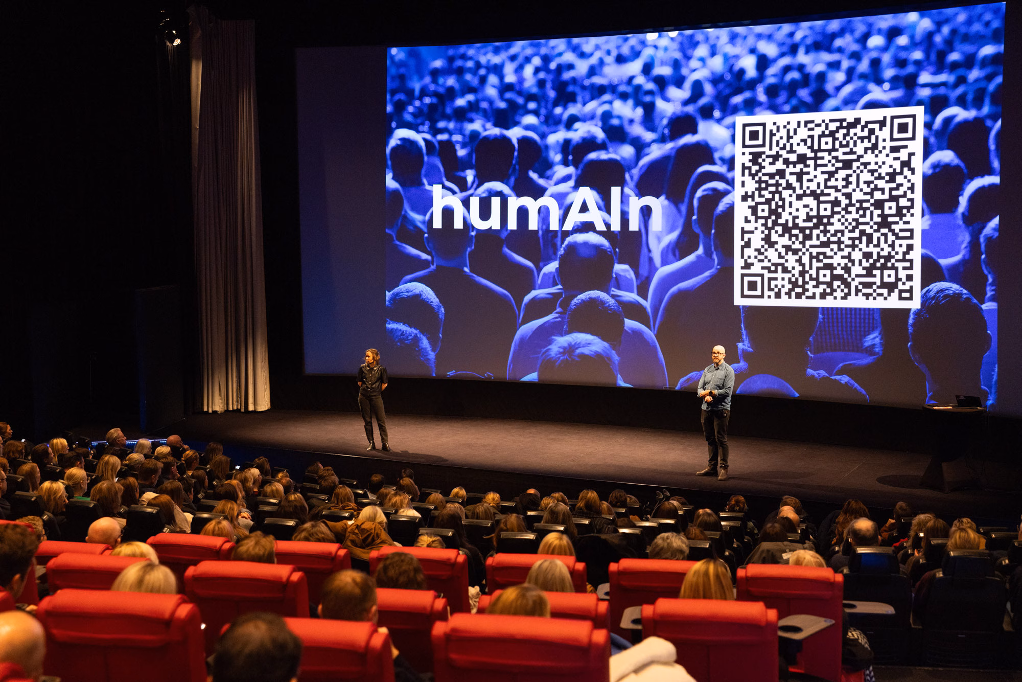 Fullsatt biosalong under AI Day 2025 på Filmstaden Sergel, med humAIn Academys logotyp på duken och värdarna på scen.
